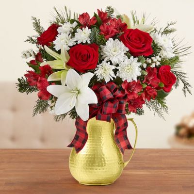 EXCLUSIVE Our spirited new bouquet captures the warmth and charm of Christmas in the county. Festive red & white blooms are gathered with holiday greens and a plaid ribbon for a rustic finishing touch. Designed in our keepsake hammered bell pitcher, featuring a mirror-polished finish, this seasonal beauty stands out in any holiday décor—from cozy cottage to formal elegance.