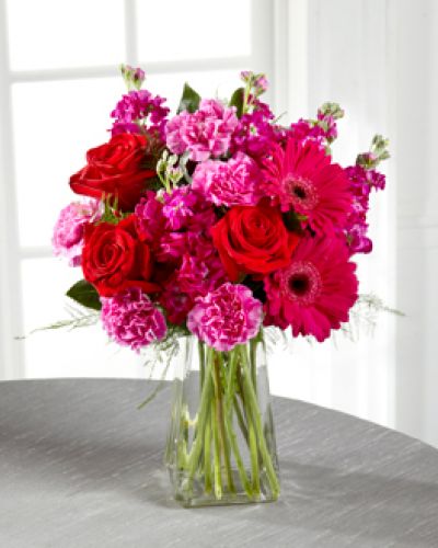 The power of pink is packed into one beautifully blushing bouquet to make your recipient's day one they will never forget! Red roses make the hot pink petals of carnations, fuchsia double bloom stock, and gerbera daisies pop in this fun and fanciful flower arrangement accented with lush greens and presented in a gathered square clear glass vase.